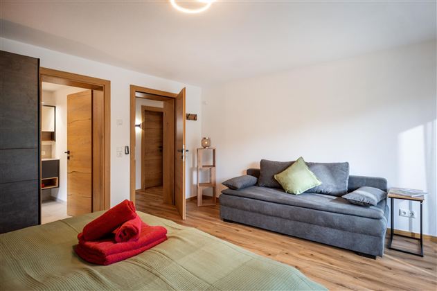 A modern room with a cozy sofa and a bed. The warm wood tones and the bright walls create an inviting atmosphere.