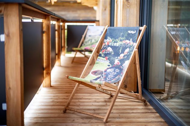 A cozy terrace with wooden lounge chairs. The chairs are decorated with colorful motifs and invite you to relax.