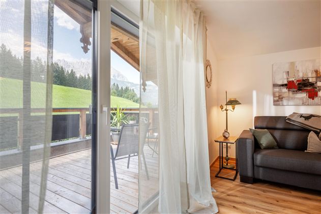 A cozy living space with a gray sofa and a floor lamp. Through the large windows, there is a view of a green landscape.