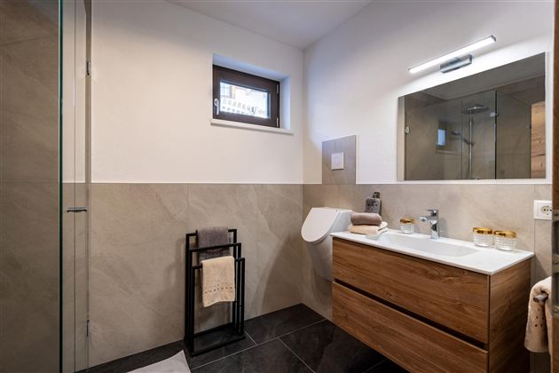 Ein modernes Badezimmer mit einer Glasdusche und einem Holzwaschbecken. Die Wände sind in neutralen Farbtönen gehalten, und es gibt einen großen Spiegel über dem Waschbecken.