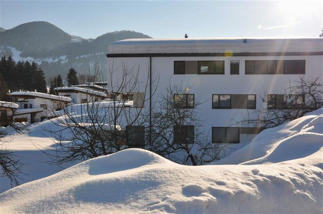 A snowy landscape with a modern building in the foreground. In the background, gentle hills and a clear sky can be seen.