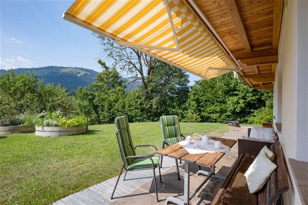 A cozy terrace area with two chairs and a table. In the background, you can see a green meadow and gentle hills.
