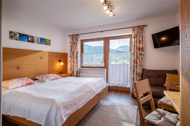A cozy hotel room with two beds and wooden decor. Large windows provide a view of the mountains and ensure plenty of daylight.