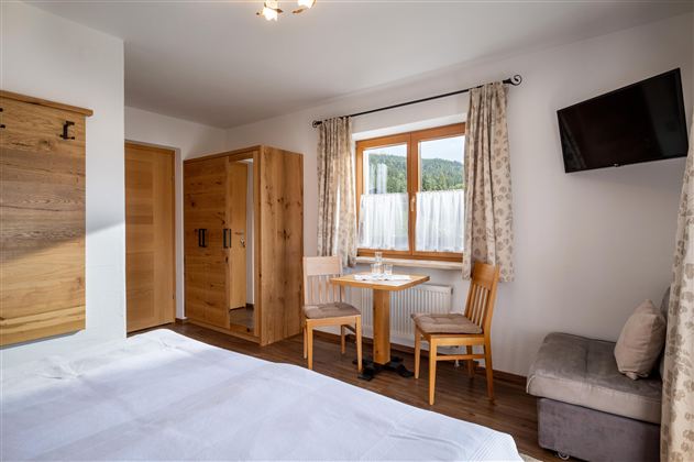 A cozy room with wood interior and a large window. There is a table with chairs and a television on the wall.