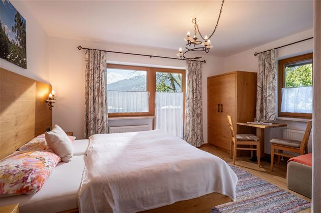 A cozy bedroom with a double bed and wooden furniture. Large windows let in plenty of daylight and offer a beautiful view outside.
