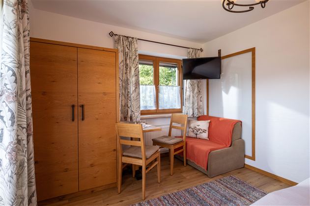 A bright room with wooden furniture and a small dining area. There is a television and large windows with curtains.