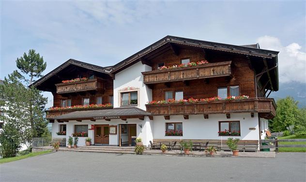 A charming wooden house with balconies and blooming flowers. It is located in a quiet setting with some trees and a clear view.