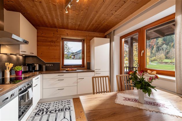 Een moderne keuken met een houten plafond en witte kasten. Een tafel met een boeket nodigt uit om te verblijven.