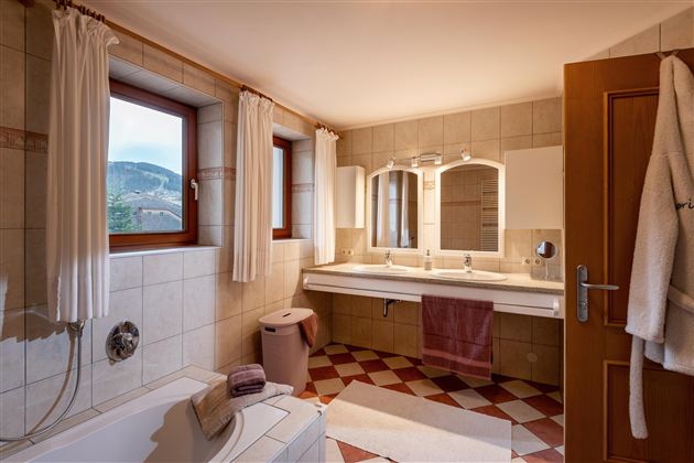 Een modern badkamer met twee wastafels en grote spiegels. Heldere ramen zorgen voor veel daglicht en een aangename sfeer.