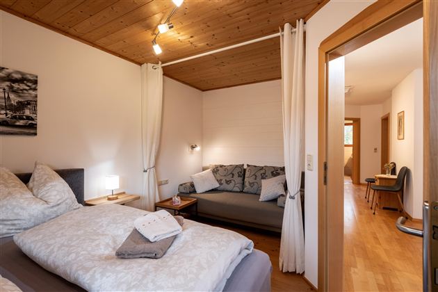 Een gezellig slaapkamer met een tweepersoonsbed en een bank. De ruimte is licht en modern ingericht, met houten bekleding en warm licht.