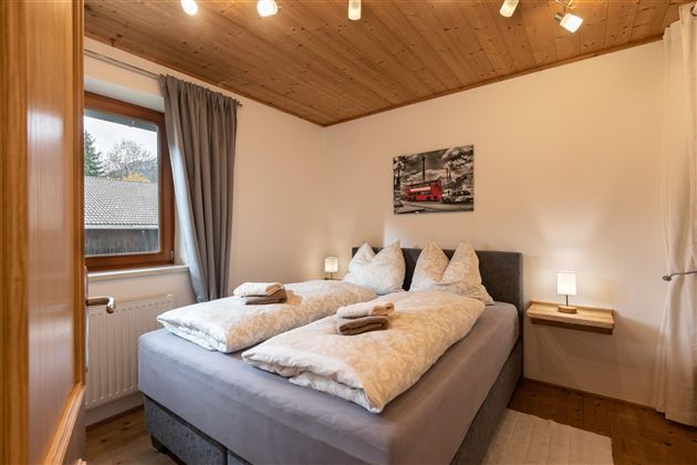 Een gezellige slaapkamer met een tweepersoonsbed en moderne nachtkastjes. Natuurlijk licht valt door het raam en creëert een uitnodigende sfeer.