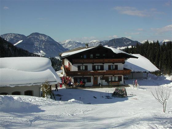 Ein gemütliches Chalet in einer verschneiten Berglandschaft. Die Umgebung ist mit frischem Schnee bedeckt und die Berge sind klar sichtbar.