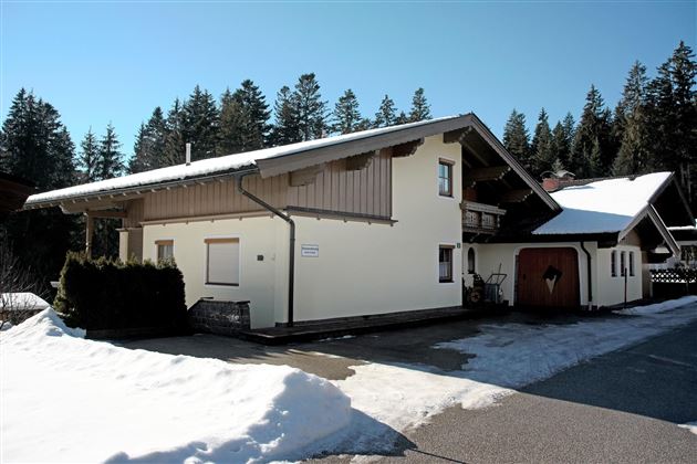 A modern house in a snow-covered landscape. In the background, high trees and blue sky can be seen.