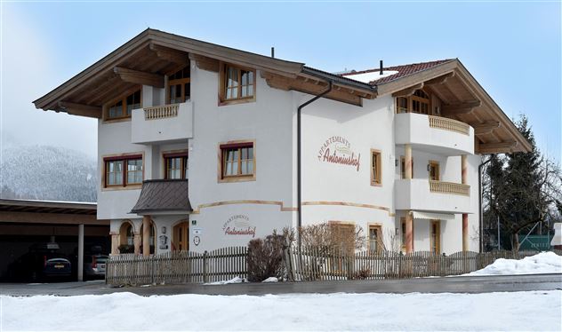 A beautiful building in Alpine style, surrounded by snow. The facade is bright with wooden decorations and classic windows.