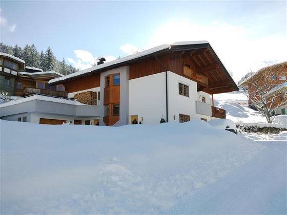 A picturesque building in alpine style, surrounded by snow. In the background, mountains can be seen.