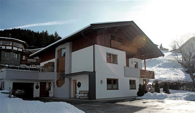 Ein modernes Haus im Schnee mit traditionellen Holzelementen. Es gibt Balkone und eine gepflegte Umgebung.