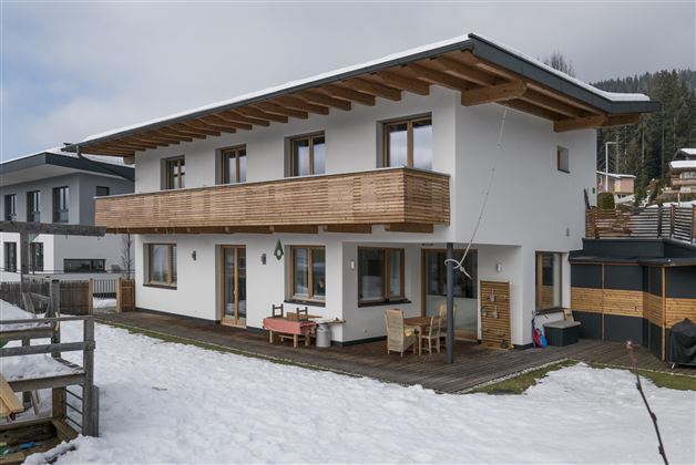 A modern house with wood siding and a spacious balcony. It is located in a winter landscape with snow.