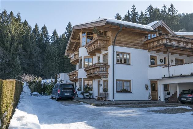 Ein charmantes alpenländisches Haus im Winter mit schneebedecktem Boden. Die Umgebung ist von dichten, grünen Wäldern umgeben.