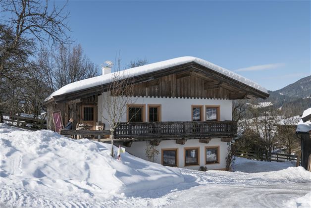 A traditional wooden house in the snow with a beautiful balcony. The sky is clear and blue, surrounded by a winter landscape.