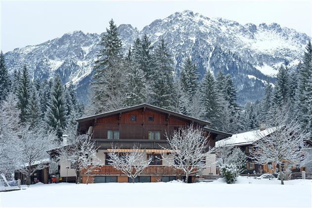 Een schilderachtig huis in de sneeuw, omringd door besneeuwde bomen. Op de achtergrond rijzen majestueuze bergen op.