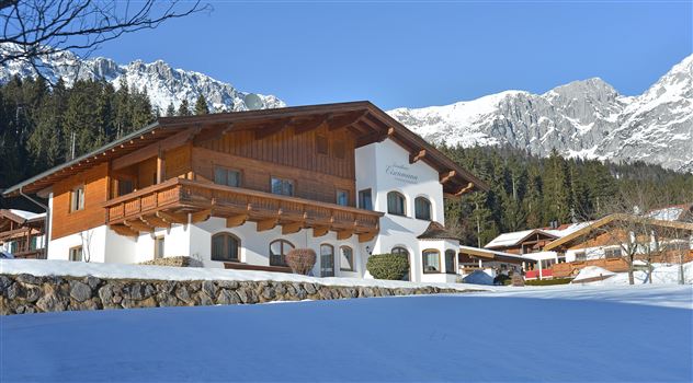 Ein gemütliches Chalet im Schnee mit einem malerischen Bergblick. Die Umgebung ist von Wäldern und Bergen umgeben.