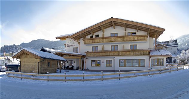 Ein charmantes Haus im alpinen Stil mit Holzverkleidung und einem Eingang. Schnee bedeckt die Umgebung und die Berge sind im Hintergrund sichtbar.