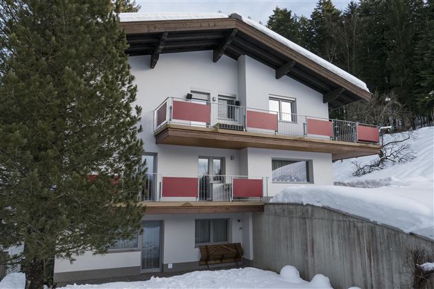 A modern building in the snow with balconies. Surrounded by trees and a peaceful winter landscape.