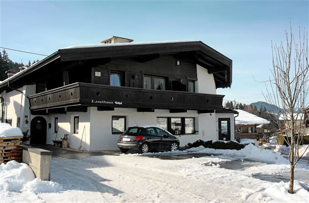 A cozy, multi-story house in the snow with a car in front. Snow-covered mountains are visible in the background.