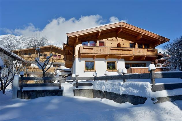 Eine malerische Winterlandschaft mit schneebedeckten Hütten. Der Himmel ist blau und die Berge sind im Hintergrund sichtbar.