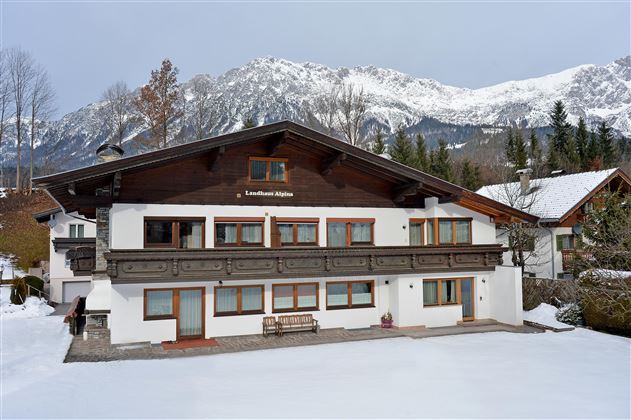 A charming wooden house in the snow with a view of snow-covered mountains. The surroundings are calm and picturesque.
