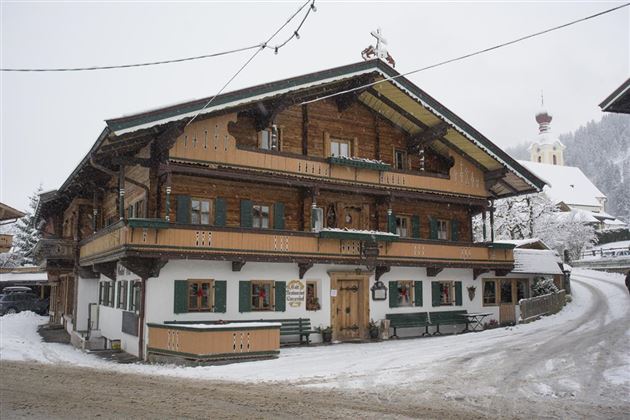 Ein traditionelles Holzhaus in einem verschneiten Dorf. Die gesamte Umgebung ist mit Schnee bedeckt, und die Architektur ist typisch für alpine Regionen.