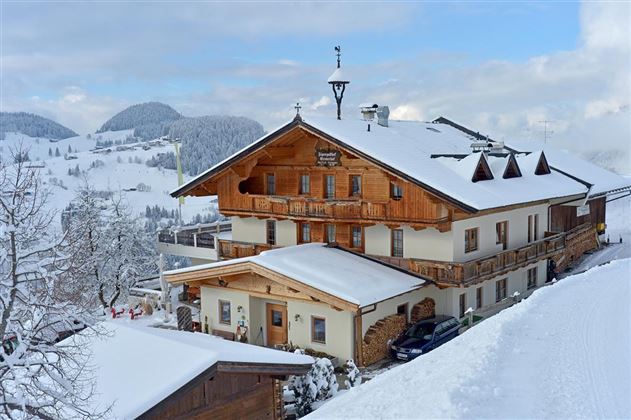 Ein charmantes, traditionelles Haus im Winter mit einer schneebedeckten Landschaft. Die Umgebung zeigt sanfte Hügel und einen klaren Himmel.