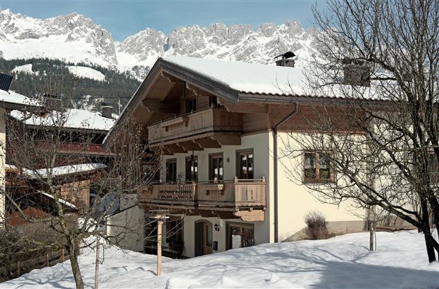 A charming house covered in snow in winter. Majestic mountains can be seen in the background.
