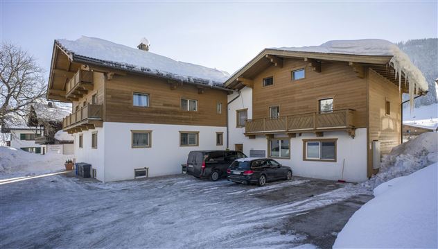 A building in the snow with two houses on top of it. In front of the houses, several cars are parked on a frozen surface.