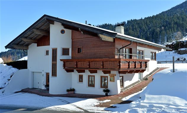A beautiful chalet in the snow with a wooden balcony. In the background, snow-covered mountains can be seen.