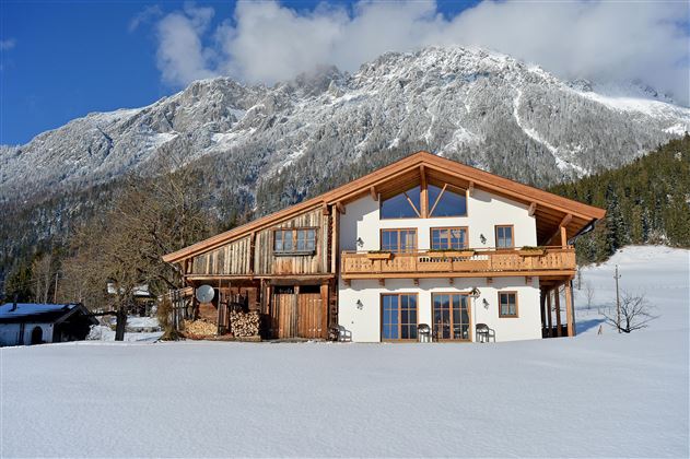 Ein wunderschönes Chalet inmitten einer verschneiten Landschaft. Im Hintergrund ragen beeindruckende Berge unter einem klaren Himmel.