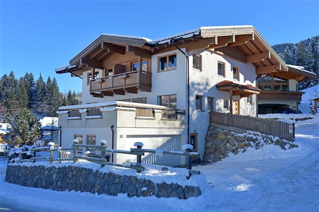 A modern house in the snow, surrounded by trees and a picturesque winter landscape. The architecture blends traditional and contemporary elements.