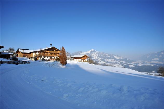 Ein malerisches Bergdorf im Winter, umgeben von schneebedeckten Landschaften. Der klare Himmel und die Berge im Hintergrund verleihen der Szene eine friedliche Atmosphäre.