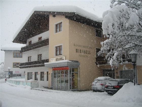 A cozy guesthouse in the snow with a large, snow-covered roof. The surroundings are wintry and picturesque.