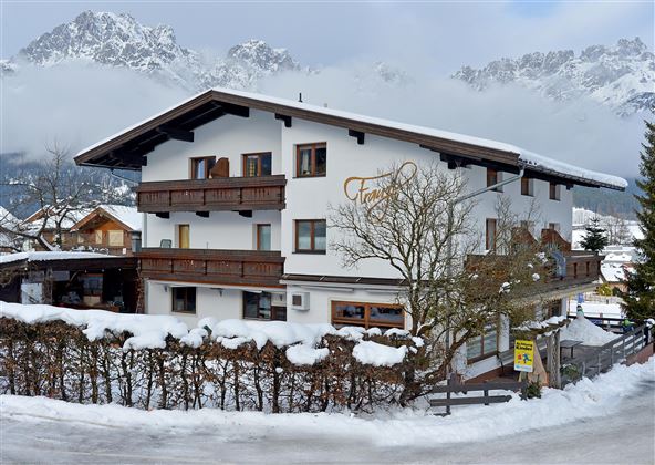 Ein charmantes, schneebedecktes Gebäude in den Alpen. Im Hintergrund sind majestätische Berge und ein bewölkter Himmel sichtbar.