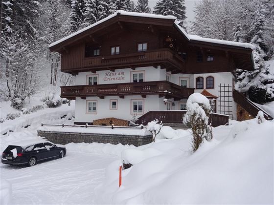 A cozy house in the snow with a balcony and wooden cladding. Surrounded by snow-covered trees and a tranquil winter landscape.