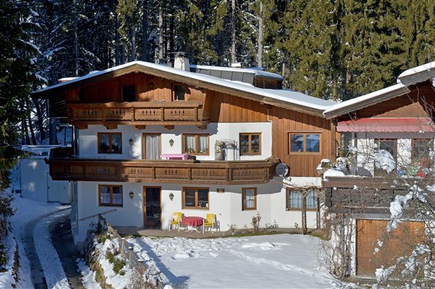 A cozy chalet in the snow, surrounded by trees. The facade is made of wood and features an inviting balcony.