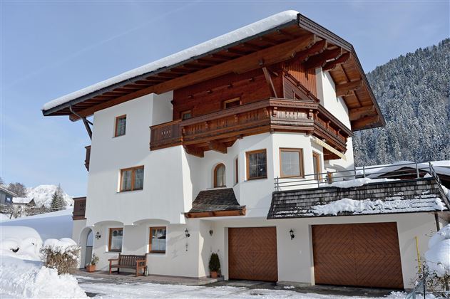 A modern house in Alpine style, surrounded by snow. The balcony and the wooden cladding give it a charming character.