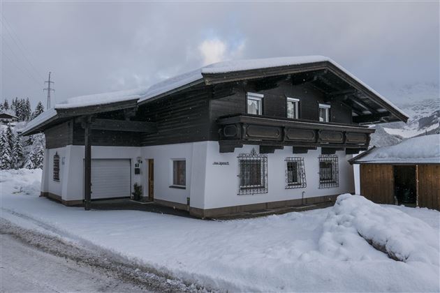 A cozy chalet in the snow with wooden cladding and balconies. Surrounded by a winter landscape.