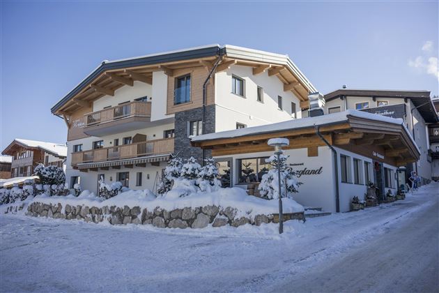 A cozy chalet in the snow, surrounded by trees. The sky is clear and the architecture is rustic.