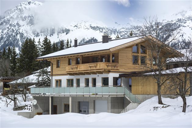 A beautiful, traditional house in the snow, surrounded by snow-covered trees. The clear blue sky enhances the winter atmosphere.