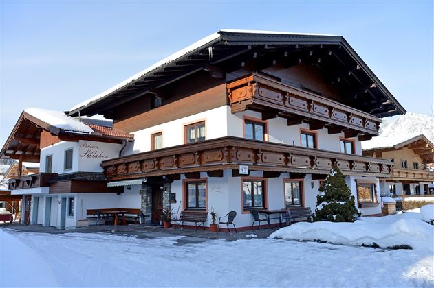 Ein gemütliches Holzgebäude im Schnee mit mehreren Etagen. Vor dem Haus stehen einige Autos auf einem verschneiten Parkplatz.