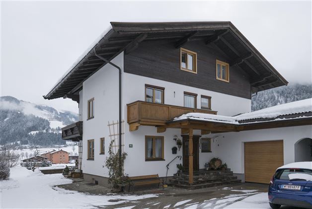 A beautiful house in the Alps, surrounded by snow-capped mountains. The facade is white with a wooden balcony.