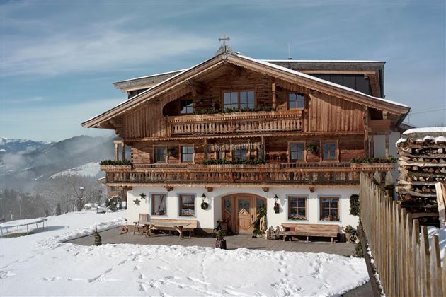 Ein traditionelles Chalet aus Holz in einer schneebedeckten Landschaft. Die Berge sind im Hintergrund sichtbar und der Himmel ist klar.