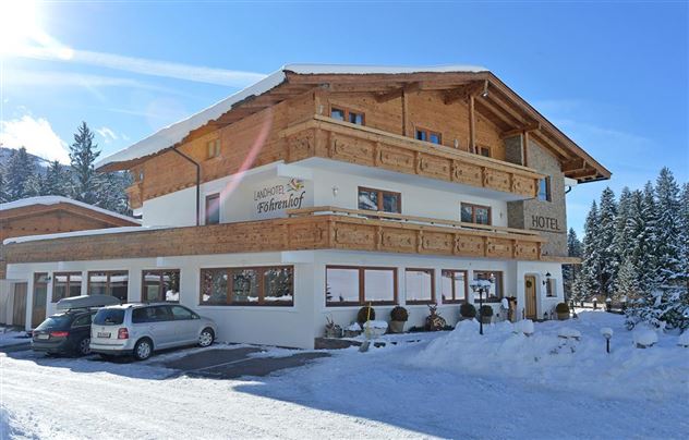 Ein charmantes Hotel mit traditioneller Holzarchitektur, umgeben von schneebedeckten Bergen. Den Gästen stehen Parkplätze vor dem Gebäude zur Verfügung.